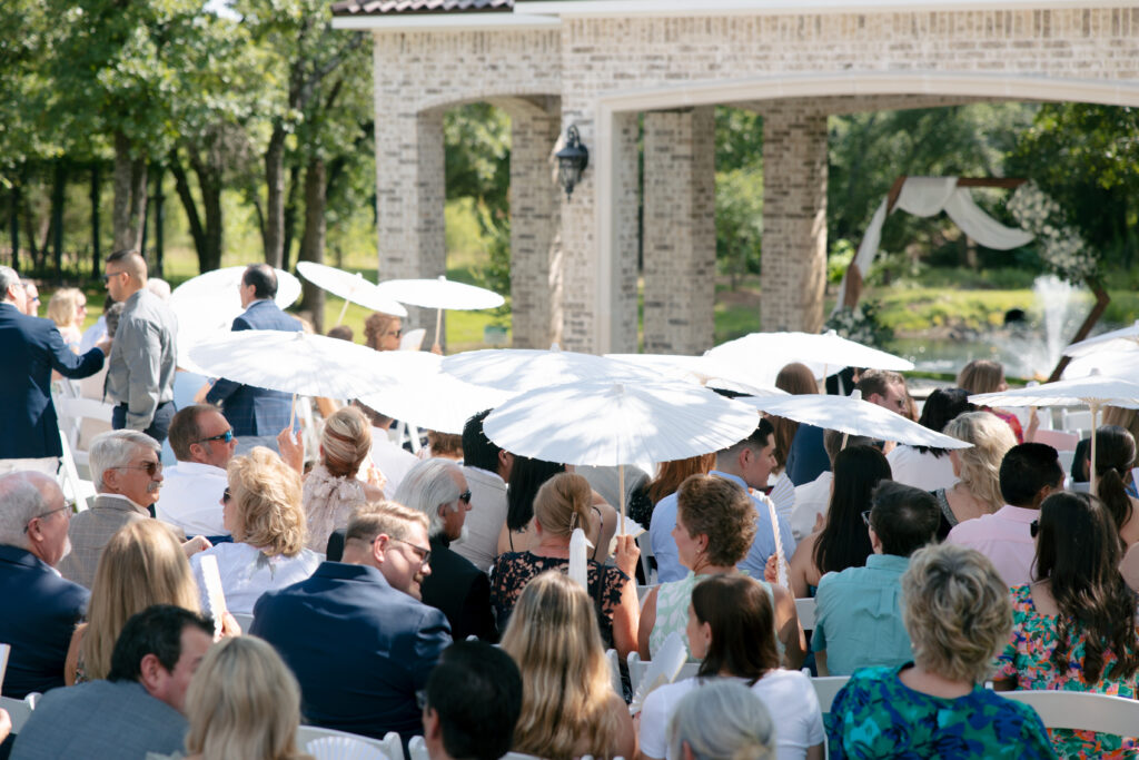 Guests sitting at the wedding ceremony holding white umbrellas.