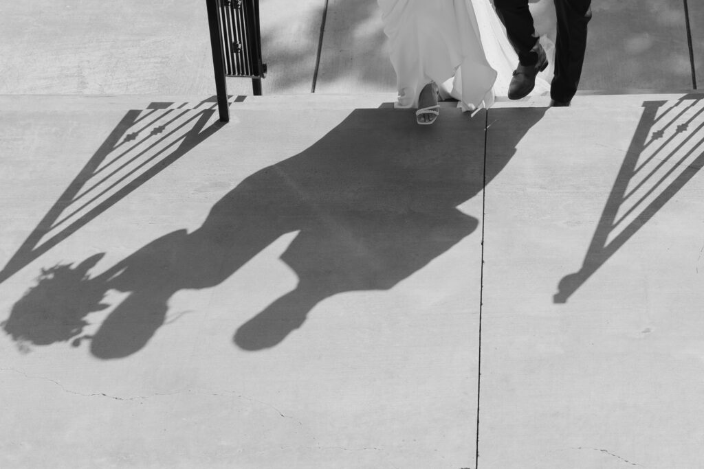 Wedding photography on with shadows on the ground of the bride and groom walking up the stairs.