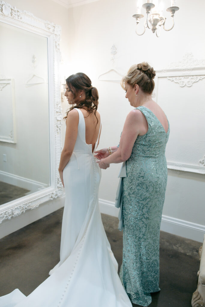 Wedding photography on film and digital of the mother of the bride buttoning the bride's dress.