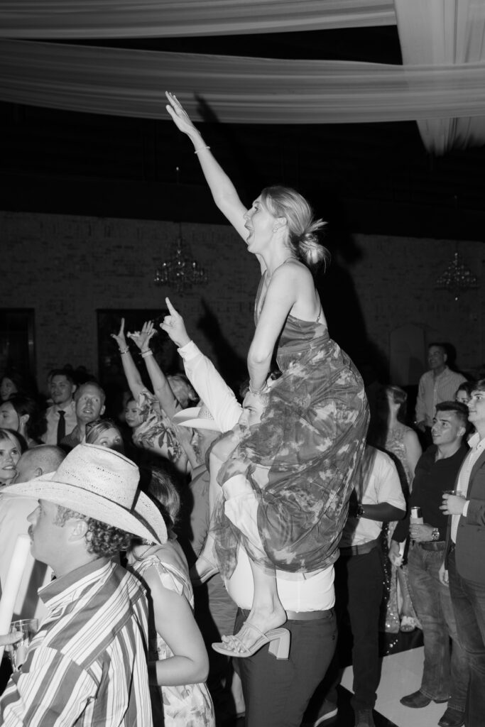 A wedding guest on someone's shoulders dancing.