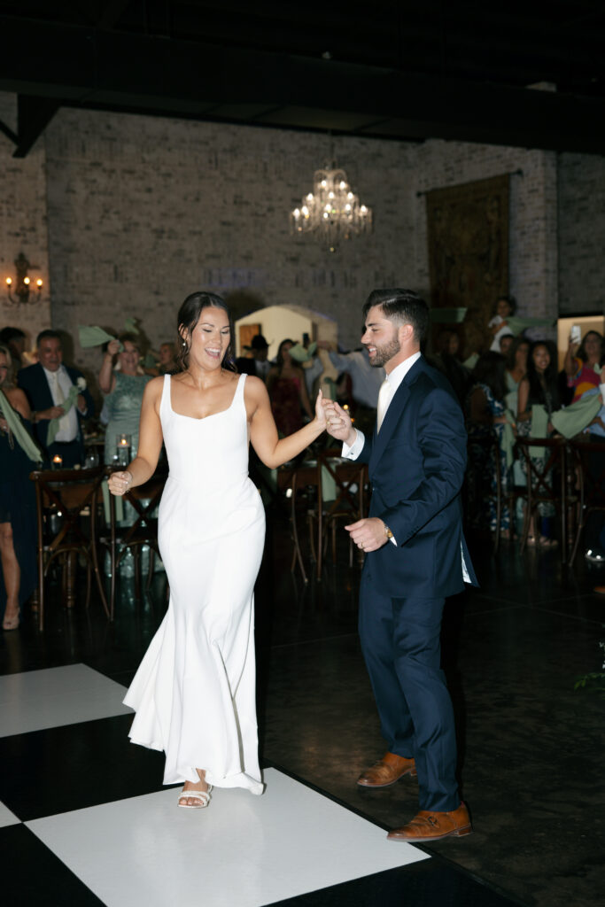 Groom holding the bride's hand as they walking onto the dance floor.