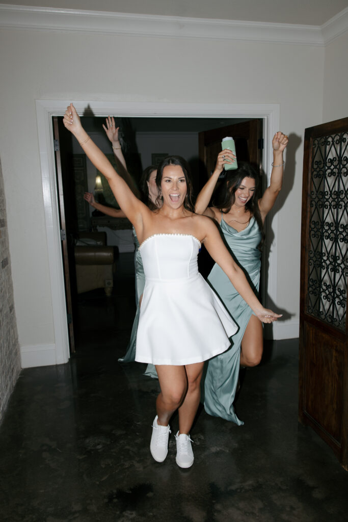 Bride with her hands in the air walking back into the reception after changing into a party dress.