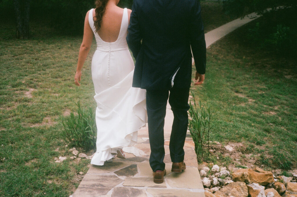 Wedding photography on film of the bride and groom walking from behind, holding hands.