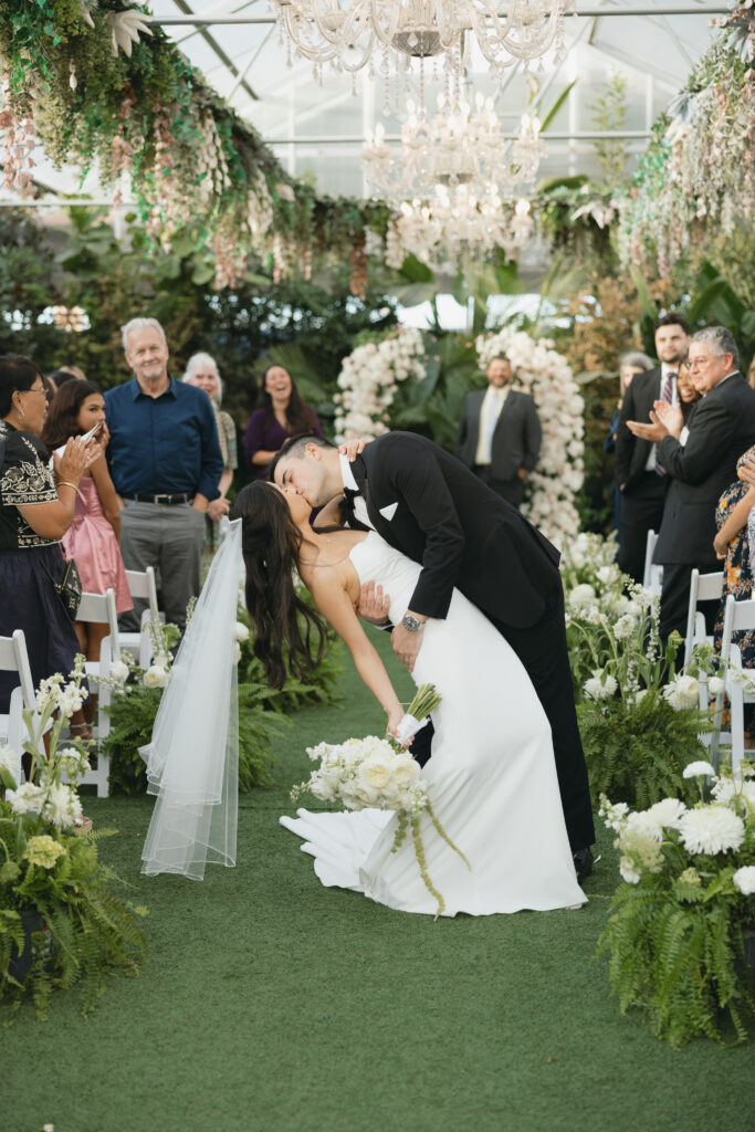 Bride and groom kissing at the end of the aisle while guests clap.