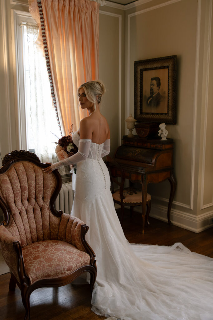 Bridal portraits of a woman at the Aldredge House posing by a vintage chair. 