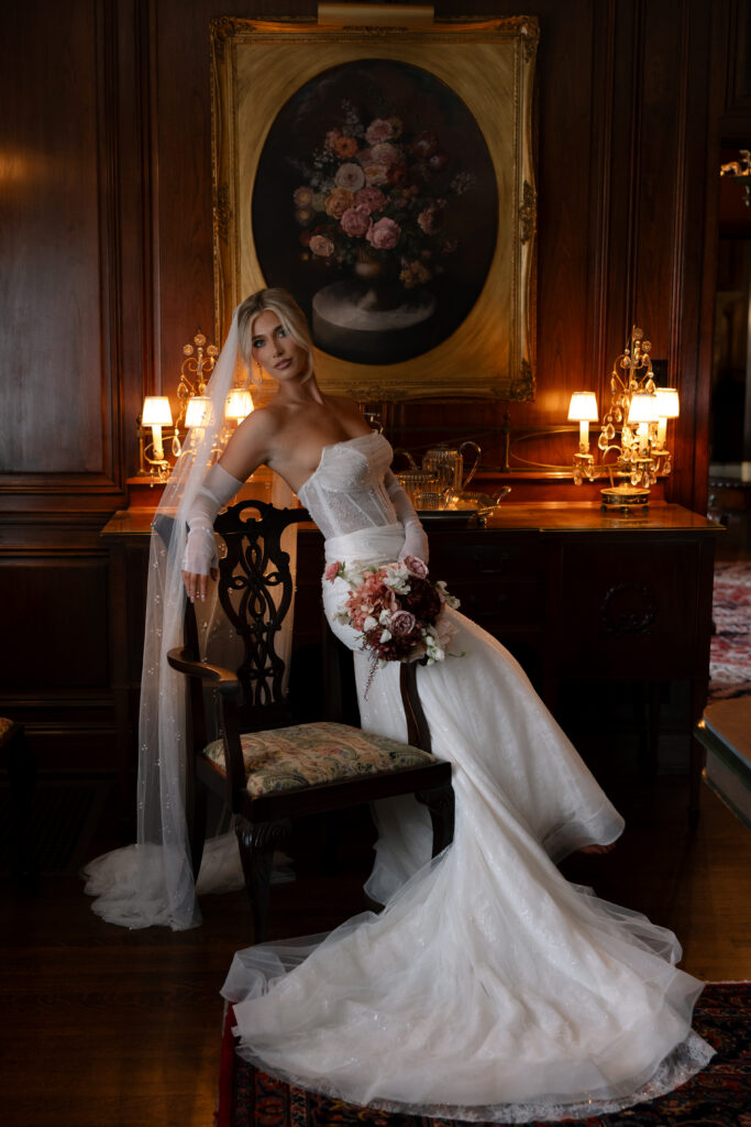 Bride posing on a chair with warm lighting in the background.