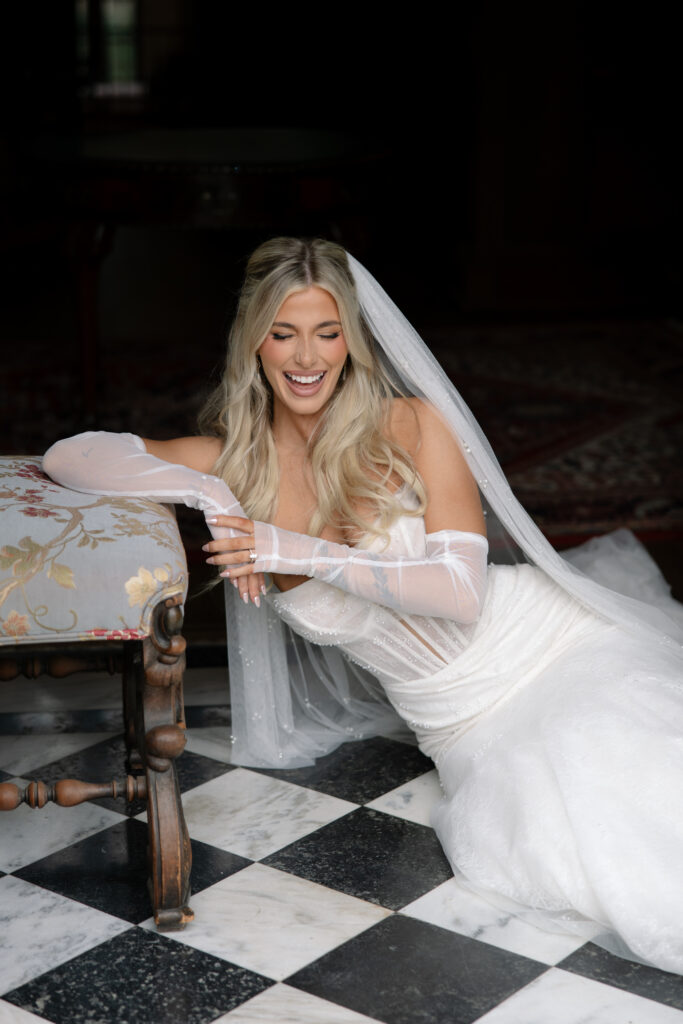 Bride smiling while sitting on the floor with checkered tiling at the Aldredge House.
