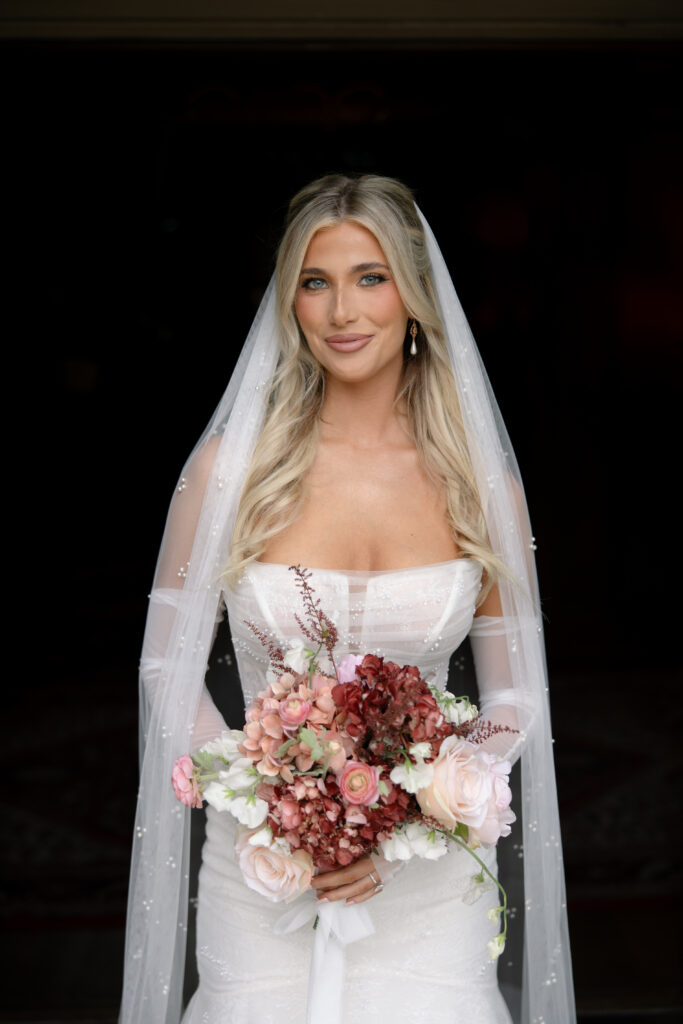 Woman smiling while holding a bouquet of flowers for bridal portraits. 