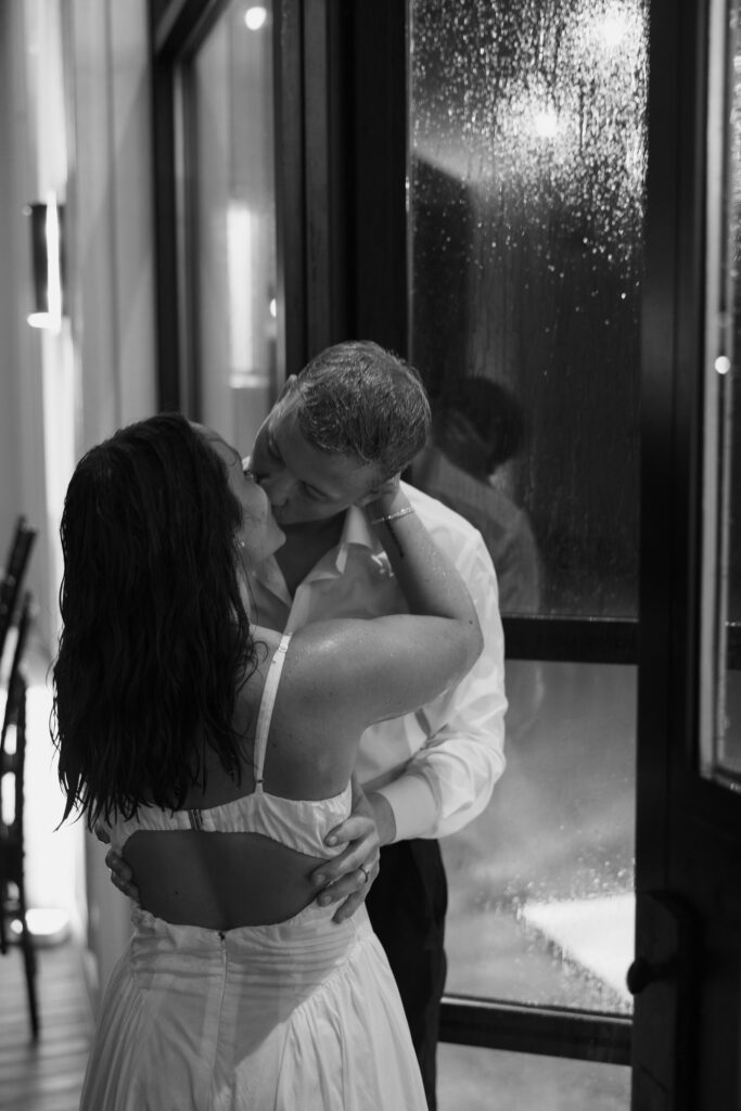 bride and groom sharing a kiss while the rain hits the window